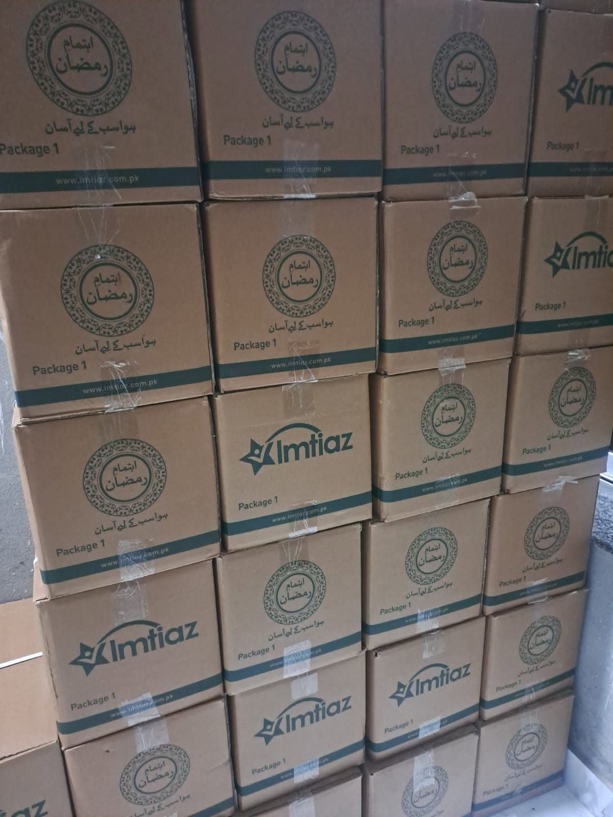 Cardboard boxes marked for Ramzan, taped shut and stacked five rows high against a wall, ready to be handed out.